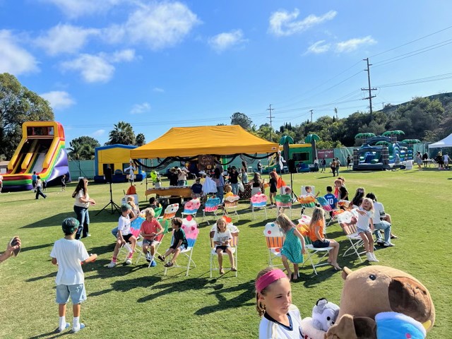 Children in a cake walk under a yellow tent, with inflatables on the field